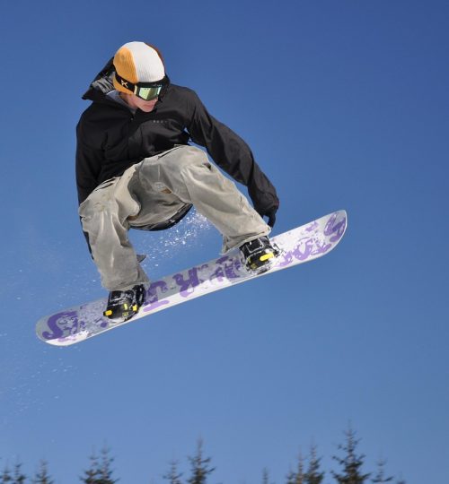 Snowboarder performing aerial jump trick against clear blue sky in winter trvel gallery