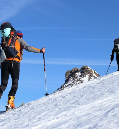 Winter sports adventurer skiing on steep snowy mountain slope with poles
